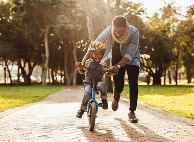 Vater unterstützt den Sohn beim Fahrrad fahren lernen im Park