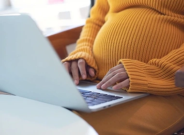 Schwangere Frau am Fenster mit Laptop